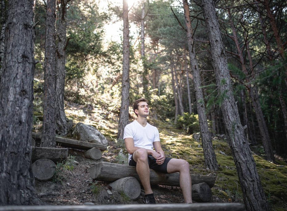 Ein Mann sitzt auf einer Holzbank im Wald.