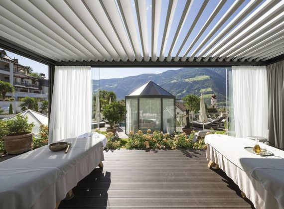 Una terrazza coperta della spa garden con due lettini, tende e vista sulle montagne.