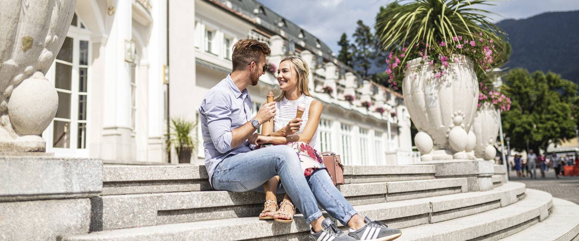 Ein Paar sitzt auf den Steinstufen vor dem Hotel und hält Eis in der Hand.