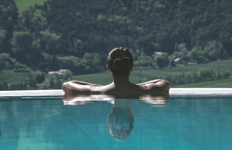 Infinity-Pool mit Bergblick im Preidlhof Eine Person lehnt im Infinity-Pool mit Blick auf die bewaldeten Berge im Hintergrund.