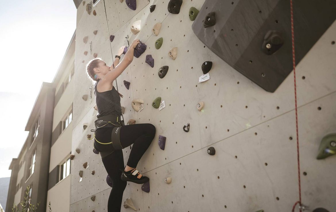 Eine Frau klettert an einer Außen-Kletterwand mit bunten Griffen.