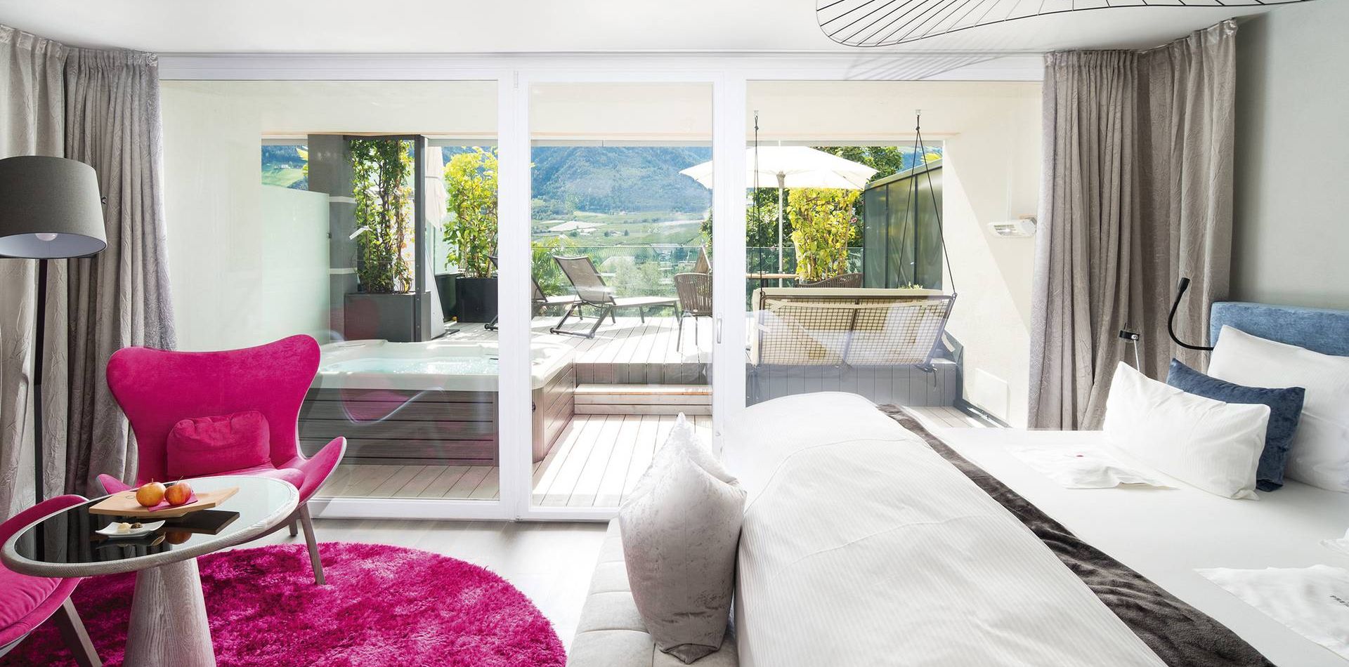 Eine helle Suite mit Bett, Sitzecke und großer Glasfront zur Terrasse mit Blick ins Grüne.