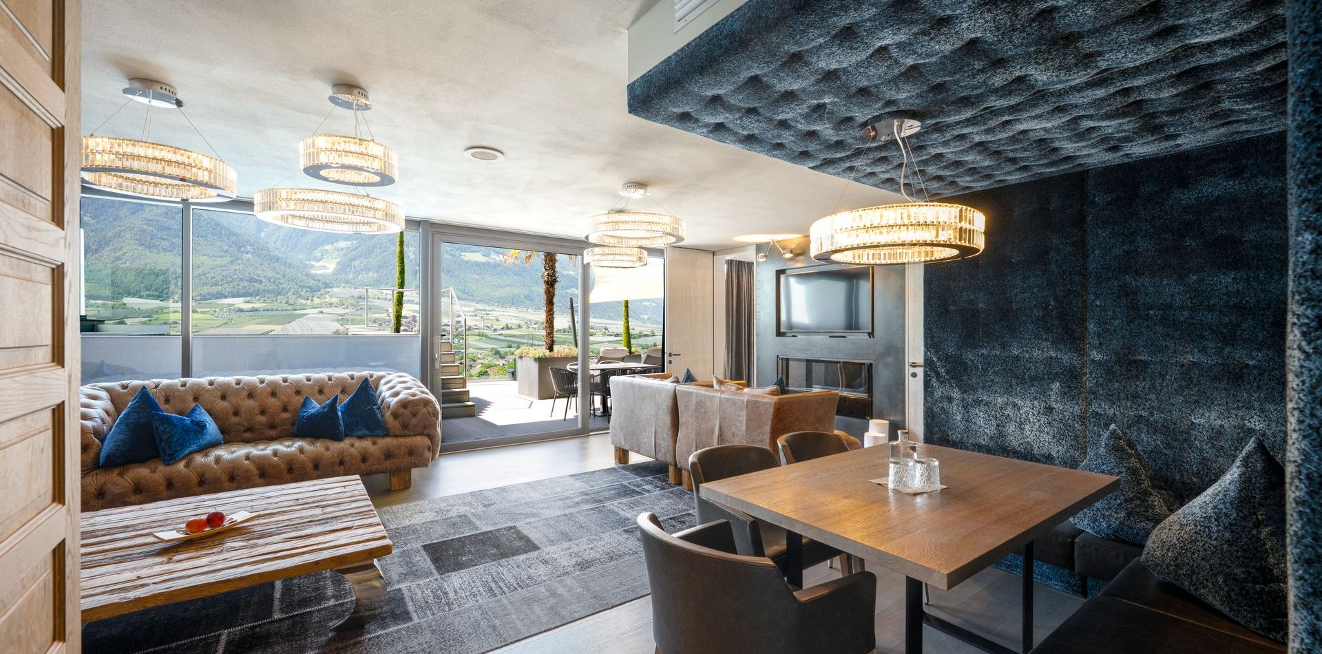 Eine elegante Penthouse Suite mit Sofaecke, Esstisch und großen Fenstern mit Blick auf die Berge.