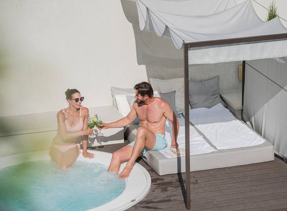 Ein Paar sitzt am kleinen Pool neben einem Himmelbett auf der Terrasse.