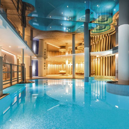 Ein heller Innenpool mit türkisfarbenem Wasser und eleganter Wellnessarchitektur im Preidlhof.