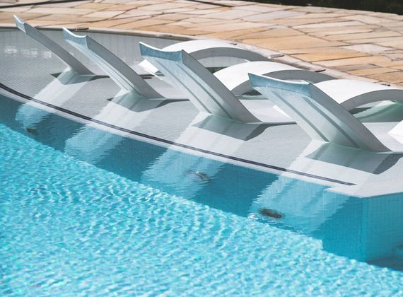 Lettini bianchi sono immersi nel bordo poco profondo di una piscina infinity turchese accanto a una terrazza in pietra.