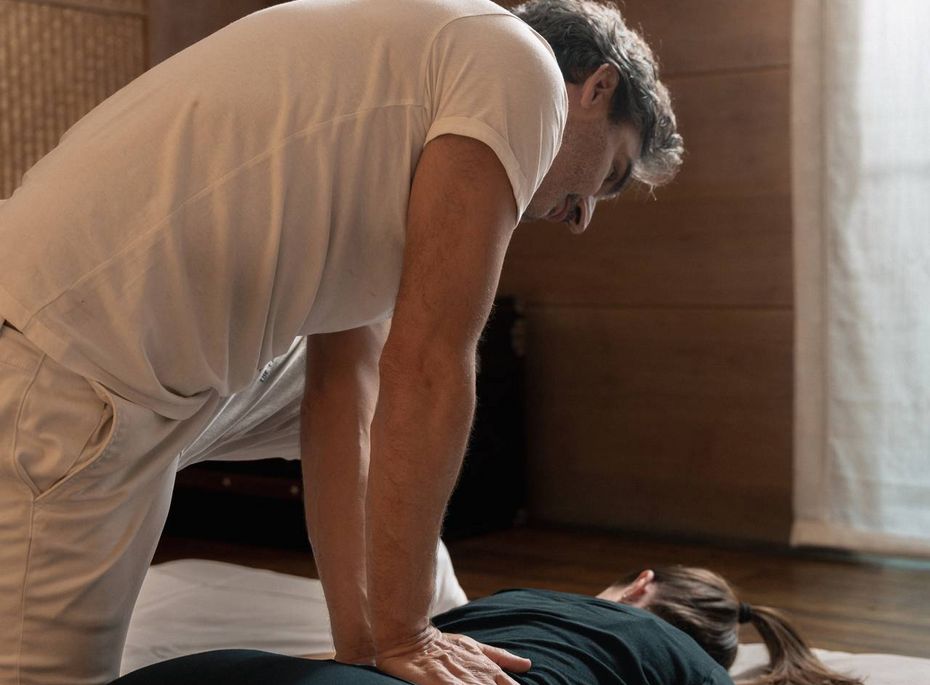 Ein Masseur behandelt eine liegende Frau in einem ruhigen Behandlungsraum des Wellnesshotels.