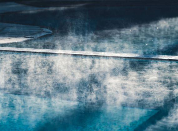 Steam rises above the thermal water in a quiet spa pool.
