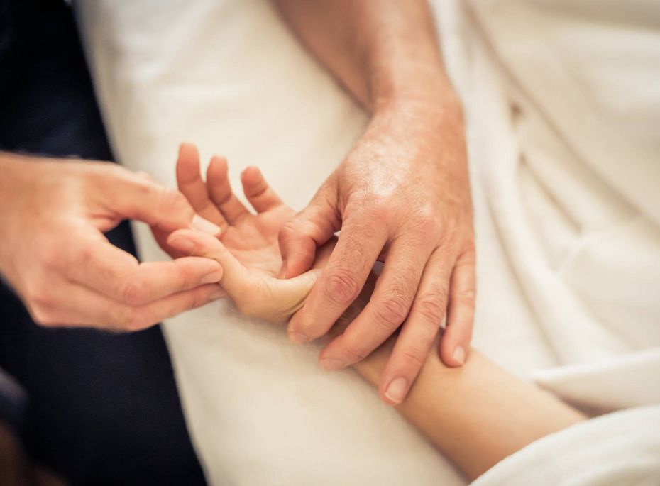 Eine Massagebehandlung an der Hand eines Gastes, während sie auf einer hellen Liege ruht.