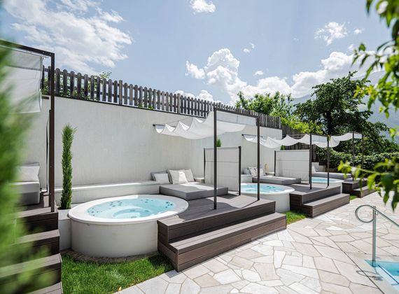 Ein Außenbereich mit Whirlpools, Liegen und Sonnensegeln neben einem Pool im Wellnesshotel.
