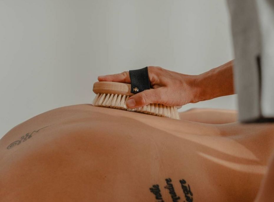 Eine Behandlung mit Bürstenmassage auf dem Rücken einer liegenden Person im Spa-Raum.