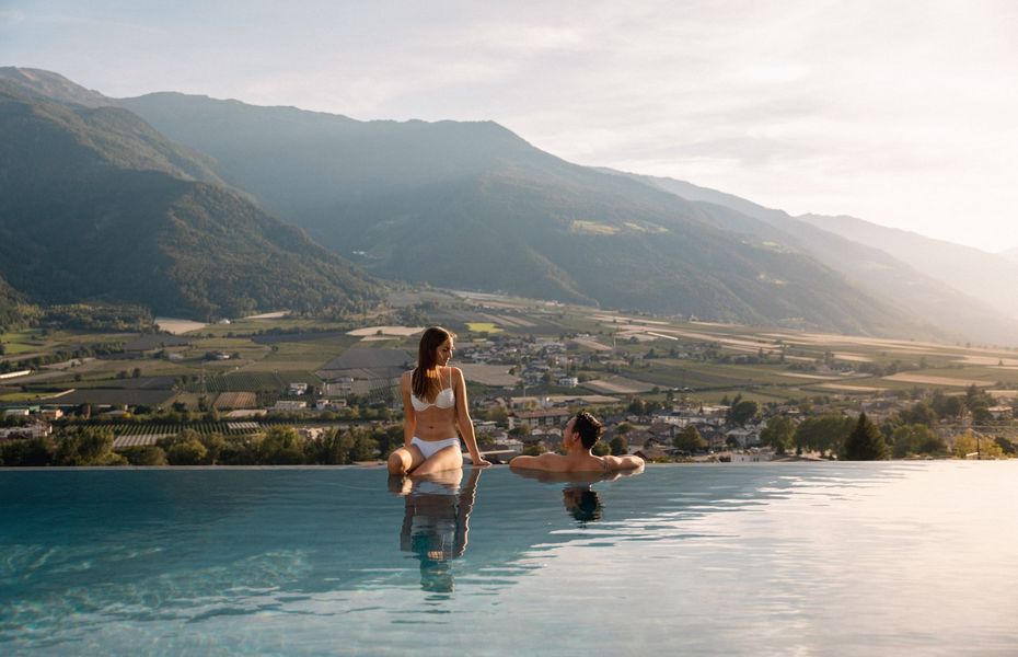 Infinity Pool im Wellnesshotel in Naturns Zwei Frauen sitzen am Rand eines Infinity-Pools mit Blick über das Tal und die Berge.