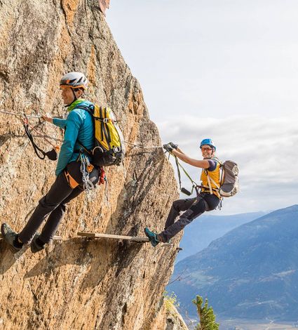 Zwei Kletterer sichern sich an einem steilen Fels-Klettersteig mit Blick ins Tal.