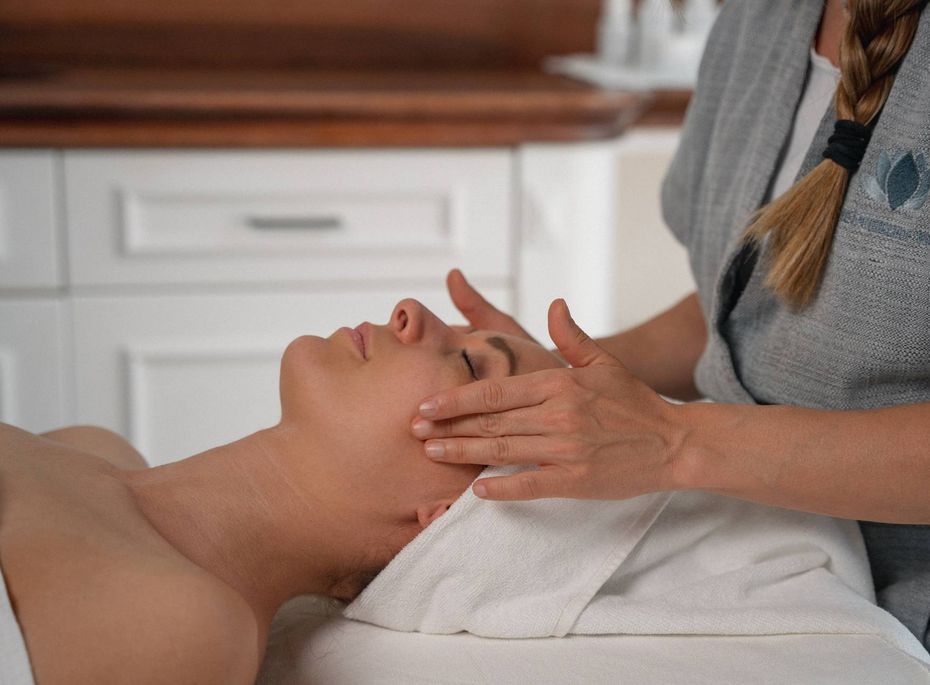 Gesichtsbehandlung im Preidlhof Wellnesshotel Eine Frau behandelt das Gesicht einer liegenden Person bei einer Wellnessanwendung auf einer Liege.