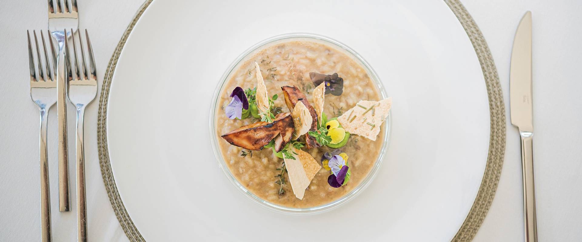 Eine Schale cremiges Risotto mit Garnitur steht auf einem gedeckten Tisch neben Messer und Besteck.
