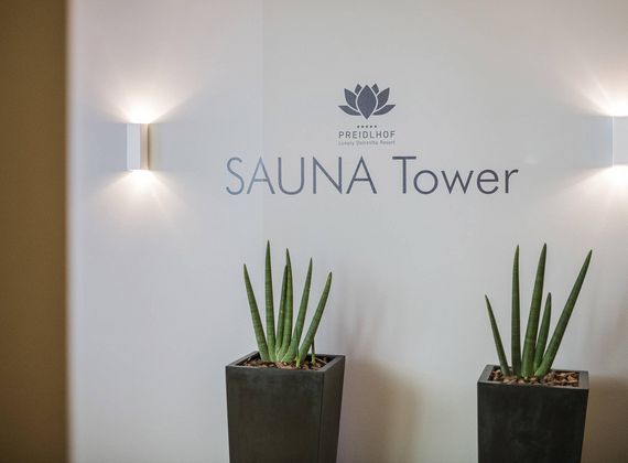 A wall with the Preidlhof logo and the words Sauna Tower above two potted plants.