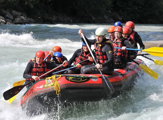 A group of rafters in helmets and life jackets paddles through choppy whitewater in an inflatable raft.