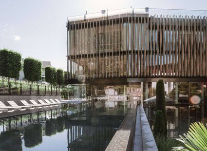 Ein Außenpool spiegelt das moderne Wellnesshotel mit Holzfassade und Liegen am Rand.