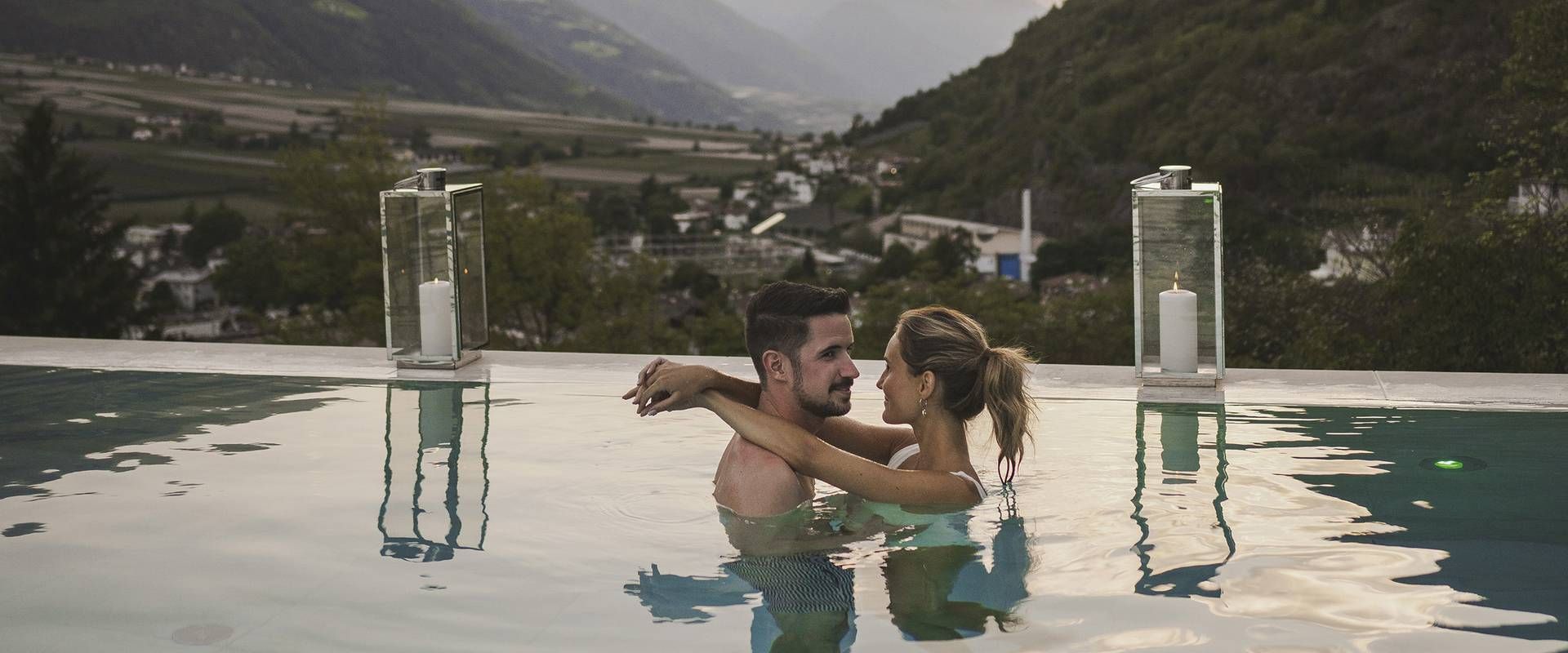 Ein Paar steht eng umschlungen im Infinity-Pool mit Blick auf das Tal und die Berge.