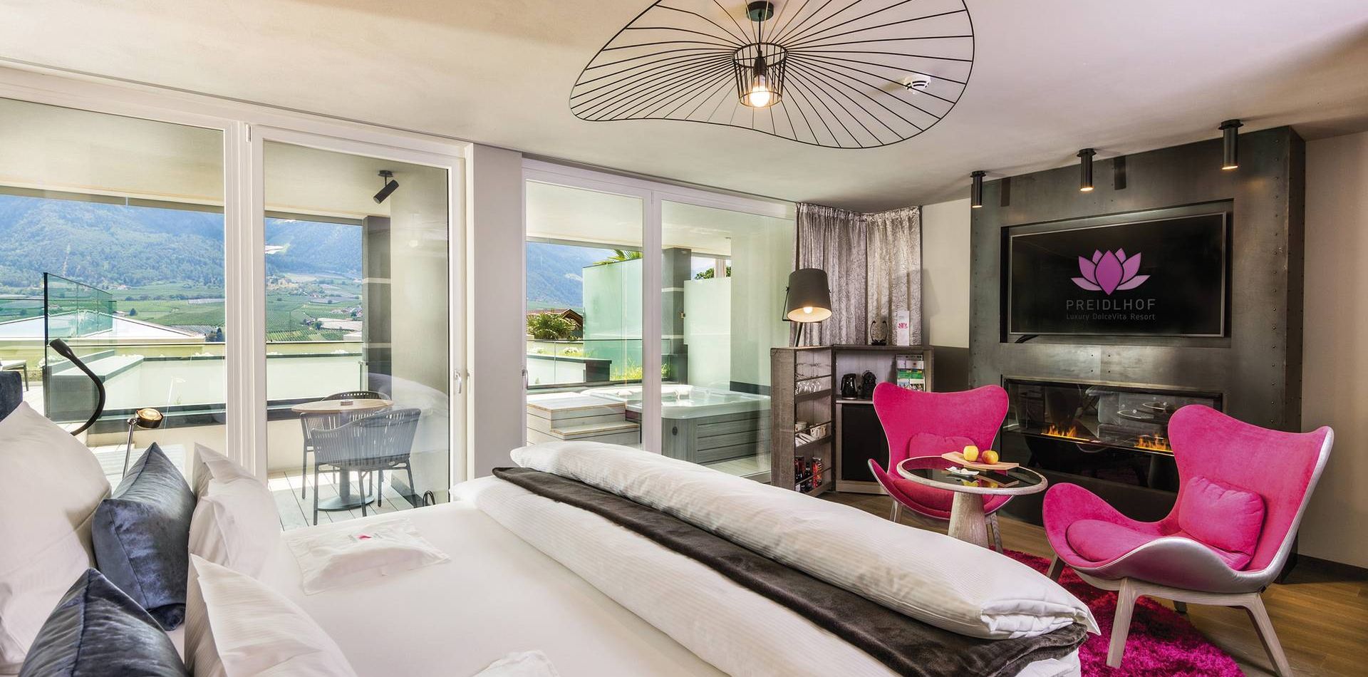 Una suite romantica con letto, poltrone rosa, camino e balcone con vista sulle montagne.