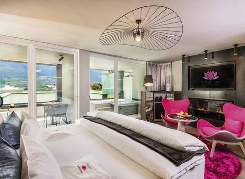 A romantic suite with a bed, pink lounge chairs, a fireplace and a balcony view of the mountains.
