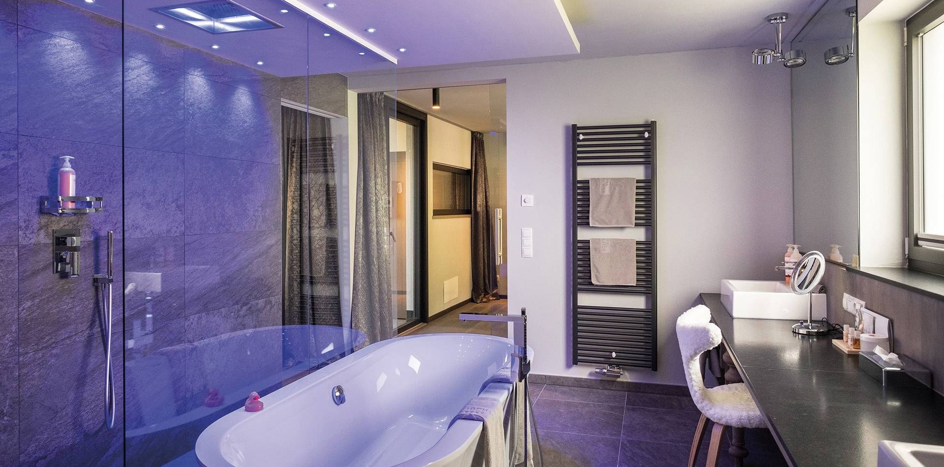 Un bagno moderno della suite con vasca freestanding, pareti in piastrelle scure, lavabo lungo e doccia in vetro.