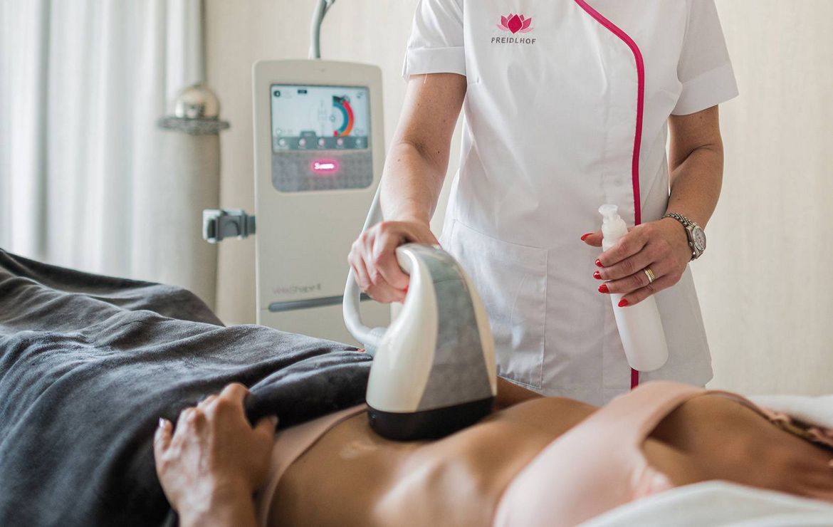 A therapist uses a handheld device on a guest's abdomen during a body contouring treatment.