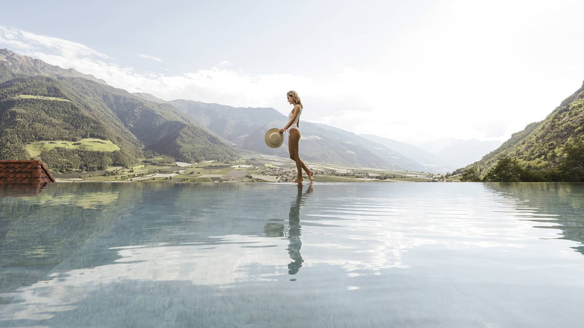 Eine Frau steht am Rand eines Infinity-Pools mit Blick auf die Berge im Wellnesshotel.