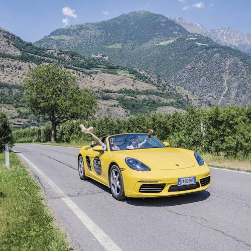 Ein gelbes Cabriolet fährt auf einer Landstraße vor einer Bergkulisse in Südtirol.