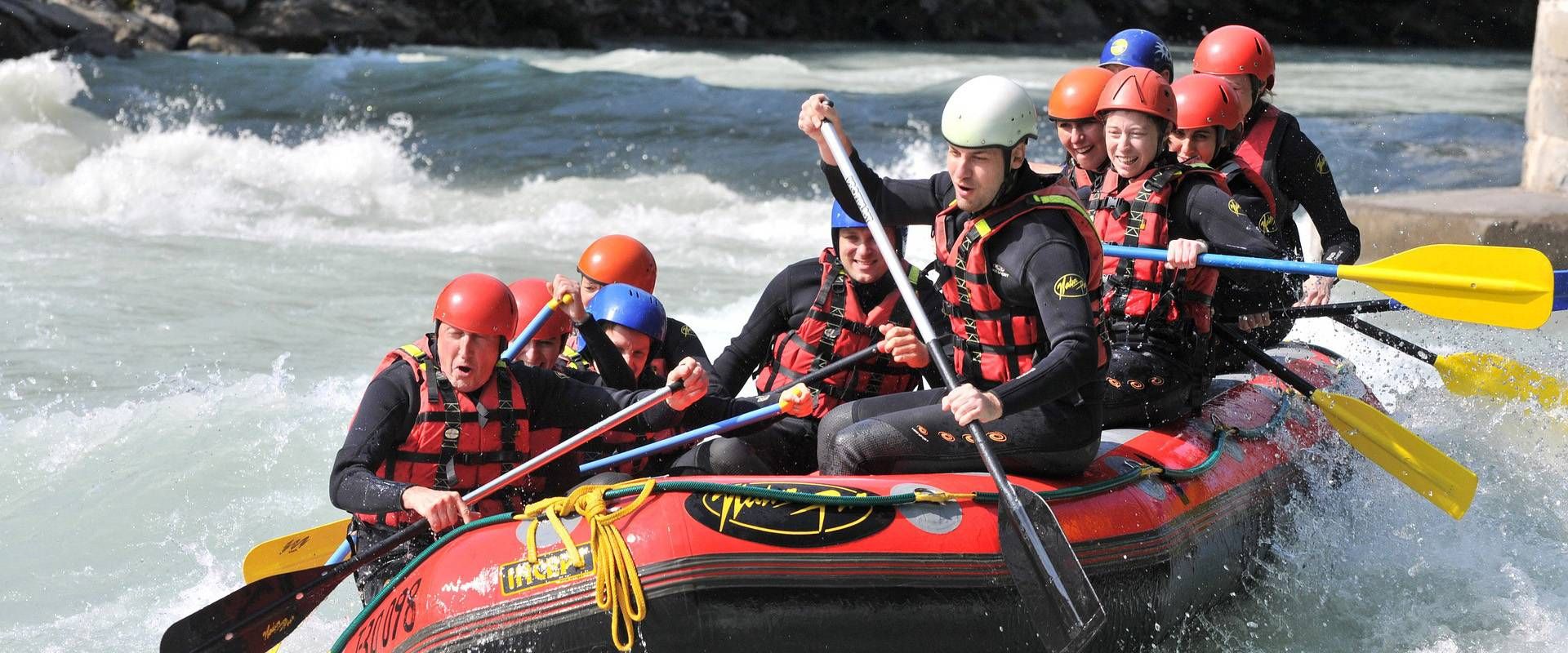 Eine Gruppe in Helmen und Schwimmwesten fährt gemeinsam in einem Raft durch Wildwasser.