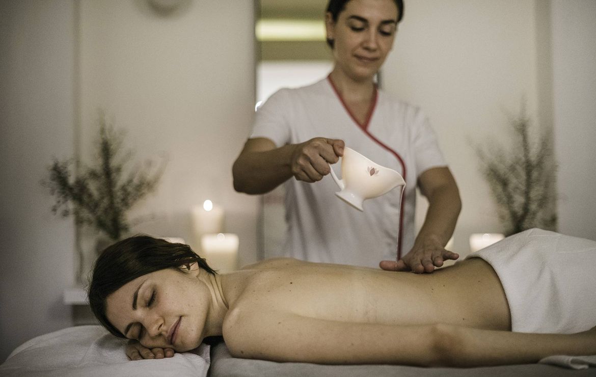 Eine Therapeutin gießt warmes Öl auf den Rücken einer liegenden Frau während einer Massage im Spa.