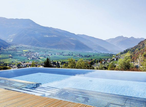 Der Infinity-Pool am Holzboden liegt vor einer weiten Tal- und Bergkulisse.
