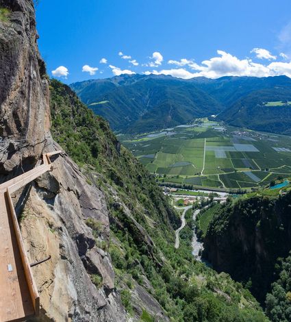 Ein gesicherter Klettersteig führt an einer steilen Felswand über das Tal mit Blick auf den Vinschgau.