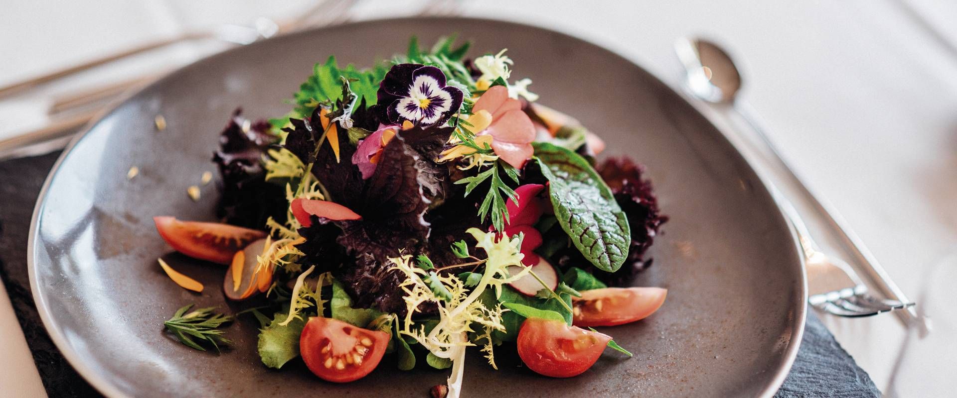 A gourmet salad with leafy greens, cherry tomatoes and edible flowers is served in a shallow bowl.
