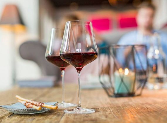 Un calice di vino rosso è appoggiato su un tavolo accanto a un piccolo piatto con grissini in una lounge soffusa.