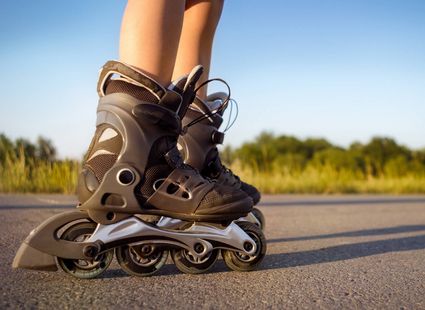 Eine Person steht mit schwarzen Inlineskates auf einer asphaltierten Straße im Freien.