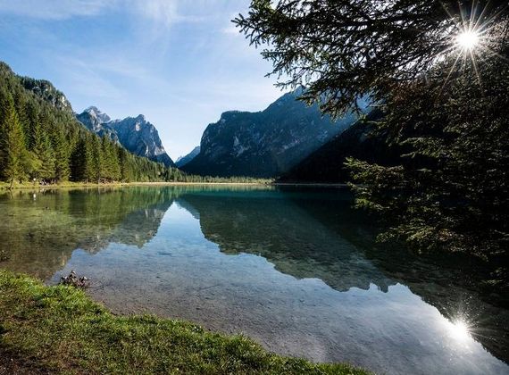 Un lago alpino limpido riflette le montagne e gli alberi in una giornata di sole.