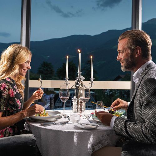 Ein Paar sitzt beim Gourmetdinner an einem gedeckten Tisch auf der Terrasse mit Blick auf die Berge.
