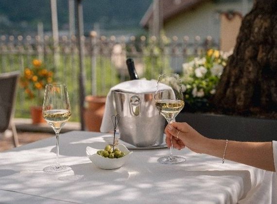 Una mano tiene un calice di vino bianco accanto a un secchiello del ghiaccio, olive e un altro calice su un tavolo all'aperto.