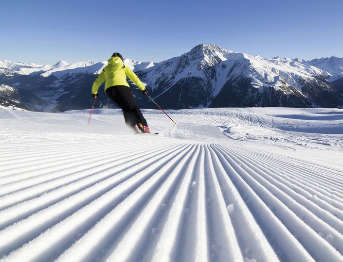 Ein Skifahrer fährt auf frisch präparierter Piste vor verschneiten Bergen in Südtirol.