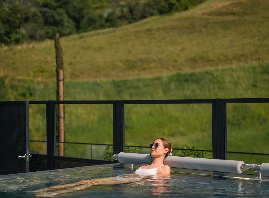 Eine Frau entspannt in einem Infinity-Pool vor einer grünen Hügellandschaft.