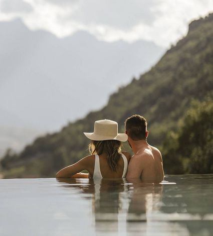 Ein Paar sitzt im Infinity-Pool und blickt auf die Berge in Südtirol.