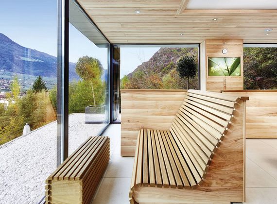 Eine helle Sauna mit Holzliegen und großen Glasflächen öffnet den Blick auf die Berge und das Tal.