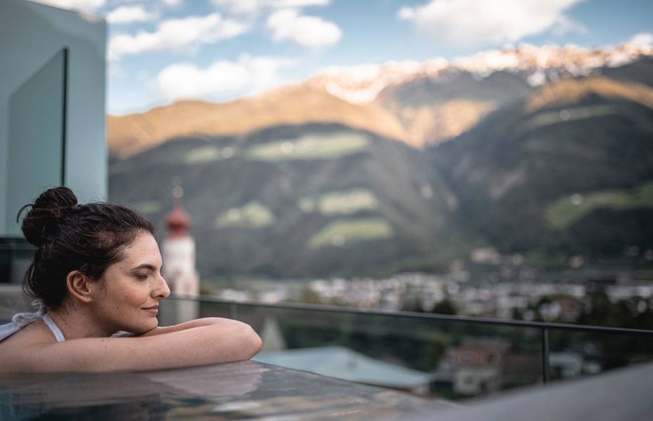 Wellnesspool mit Bergblick im Preidlhof Eine Frau lehnt am Beckenrand eines Pools mit Blick auf die Berge im Hintergrund.