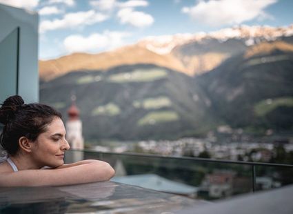 Eine Frau lehnt am Beckenrand eines Pools mit Blick auf die Berge im Hintergrund.