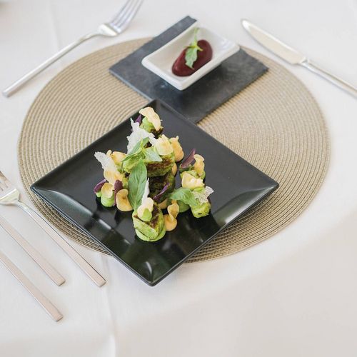 Eine feine Tellerkomposition mit Salat, Gemüse und einer kleinen Dessert- oder Saucenportion auf elegant gedecktem Tisch.