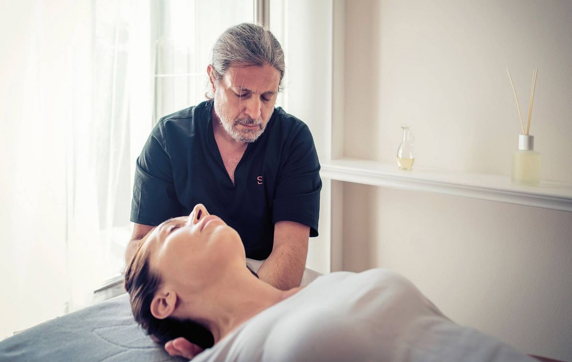 Ein Therapeut behandelt eine liegende Frau bei einer Massage in einem hellen Behandlungsraum.