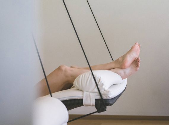 A guest rests on a suspended relaxation lounger with a pillow in a quiet spa room.