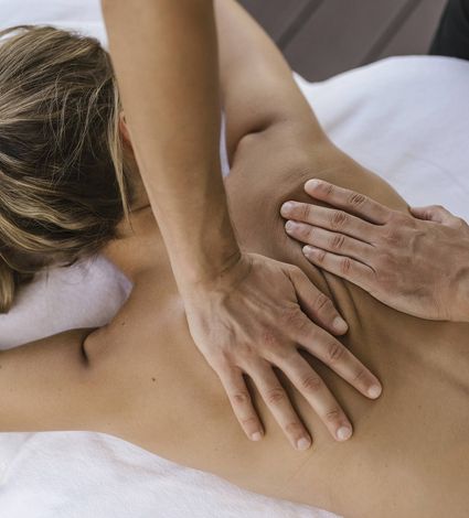 Eine Person erhält eine Massage im Spa, während zwei Hände den oberen Rücken und die Schulterpartie behandeln.