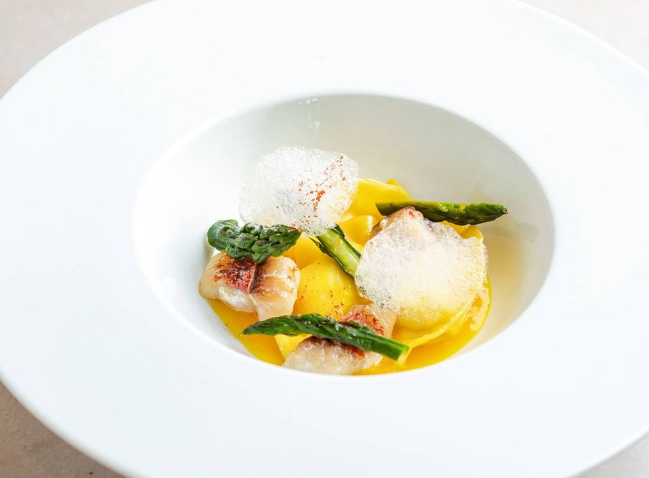 Gourmetgericht im Preidlhof in Naturns Ein fein angerichtetes Gourmetgericht mit Spargel, Kartoffelcreme und knusprigen Elementen in einem tiefen weißen Teller.